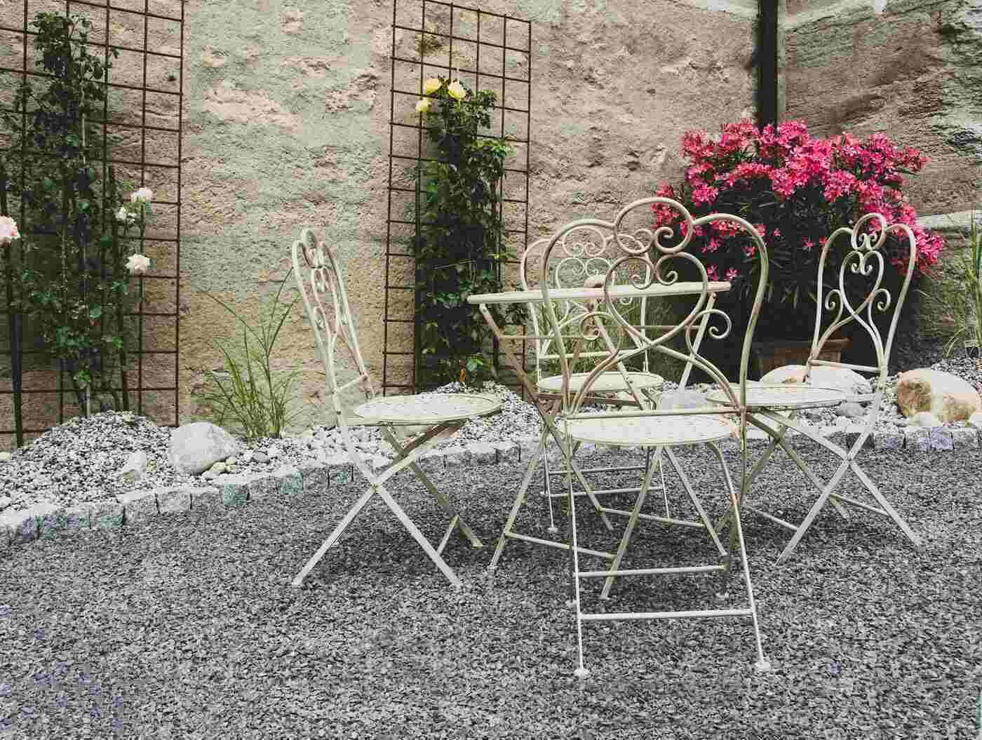 bistro en métal blanc dans une cour fleurie - les avantages du mobilier de jardin tous temps
